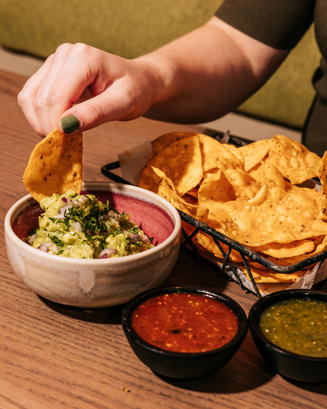 just-fried tortilla chip dipped in guacamole, with chipotle and tomatillo salsas on the side.